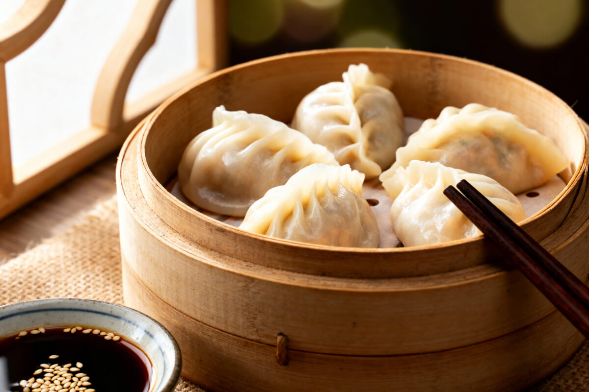 Homemade Chinese dumplings served on a ceramic plate with peanut dipping sauce, chili oil, and fresh green onions, styled with chopsticks